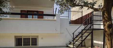 A modern building with a staircase leading to an upper level, a small window, and a tree in the foreground.