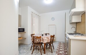 A compact kitchen with a dining table, chairs, a microwave, a sink, and a clock on the wall.