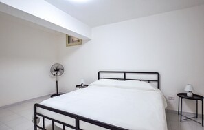 A single bed with a black frame, a bedside table with a lamp, and a floor fan.