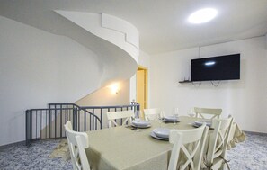 A dining area with a spiral staircase, a flat-screen TV mounted on the wall, and a table set for four.