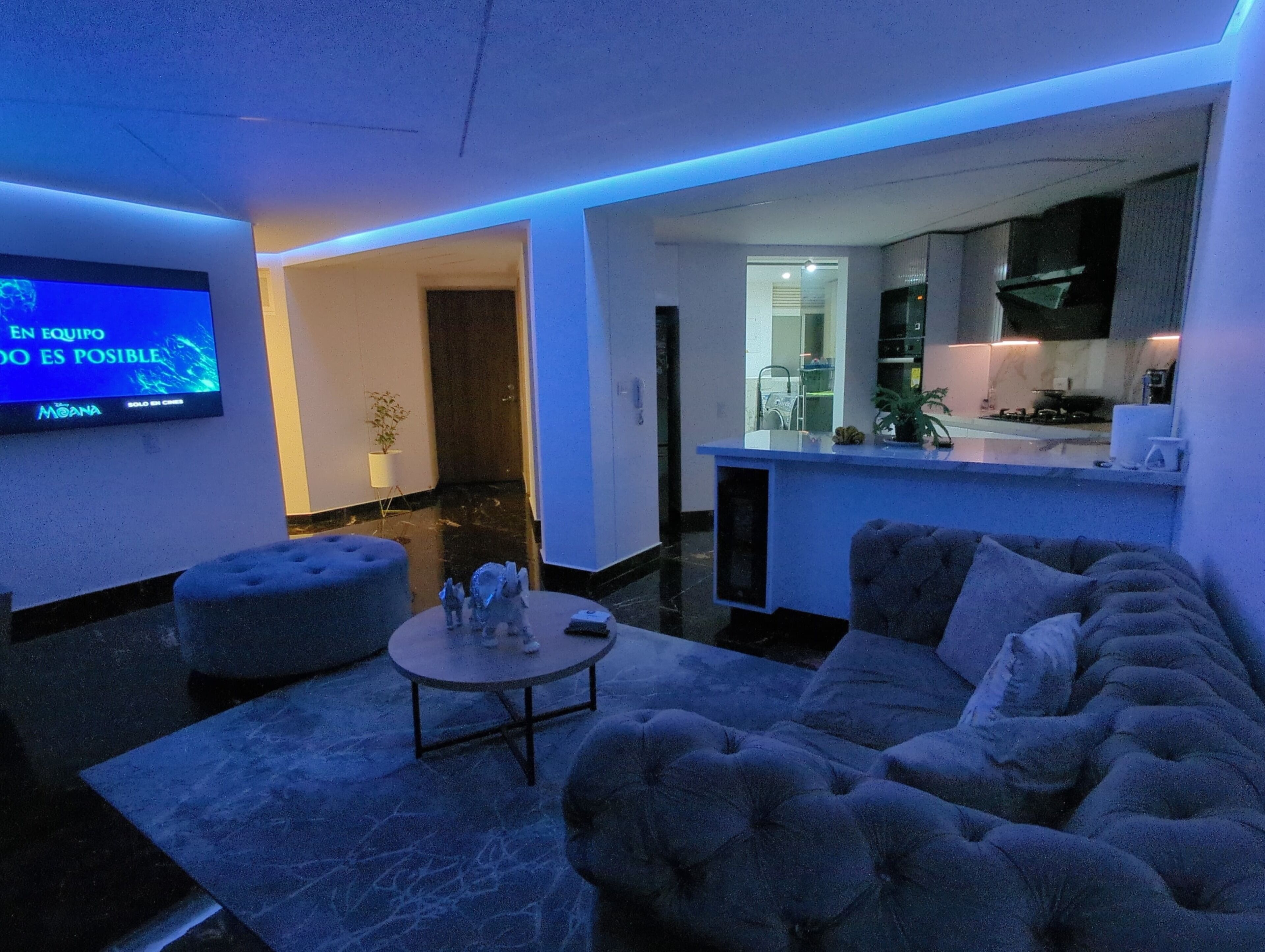 Un salon moderne avec un canapé, un pouf et un téléviseur à écran plat fixé au mur.