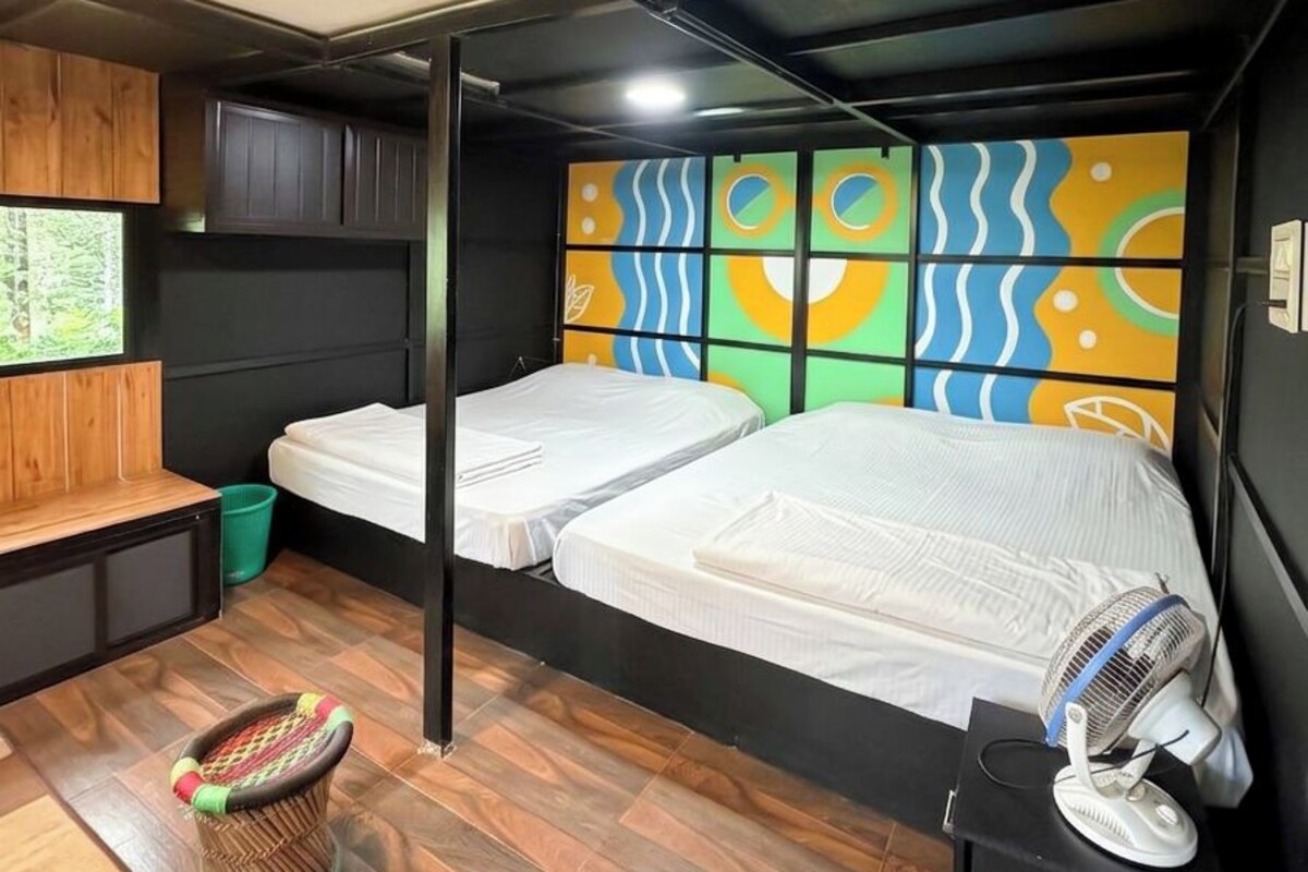 Habitación pequeña con literas, una zona de estar reducida, un ventilador y un televisor instalado en la pared.