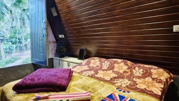 Een kamer met een bed, een houten lattenkap, een raam met uitzicht op groen en een deur.