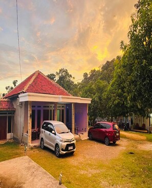 A two-story house with a red-tiled roof, a covered porch, and two cars parked in the driveway.