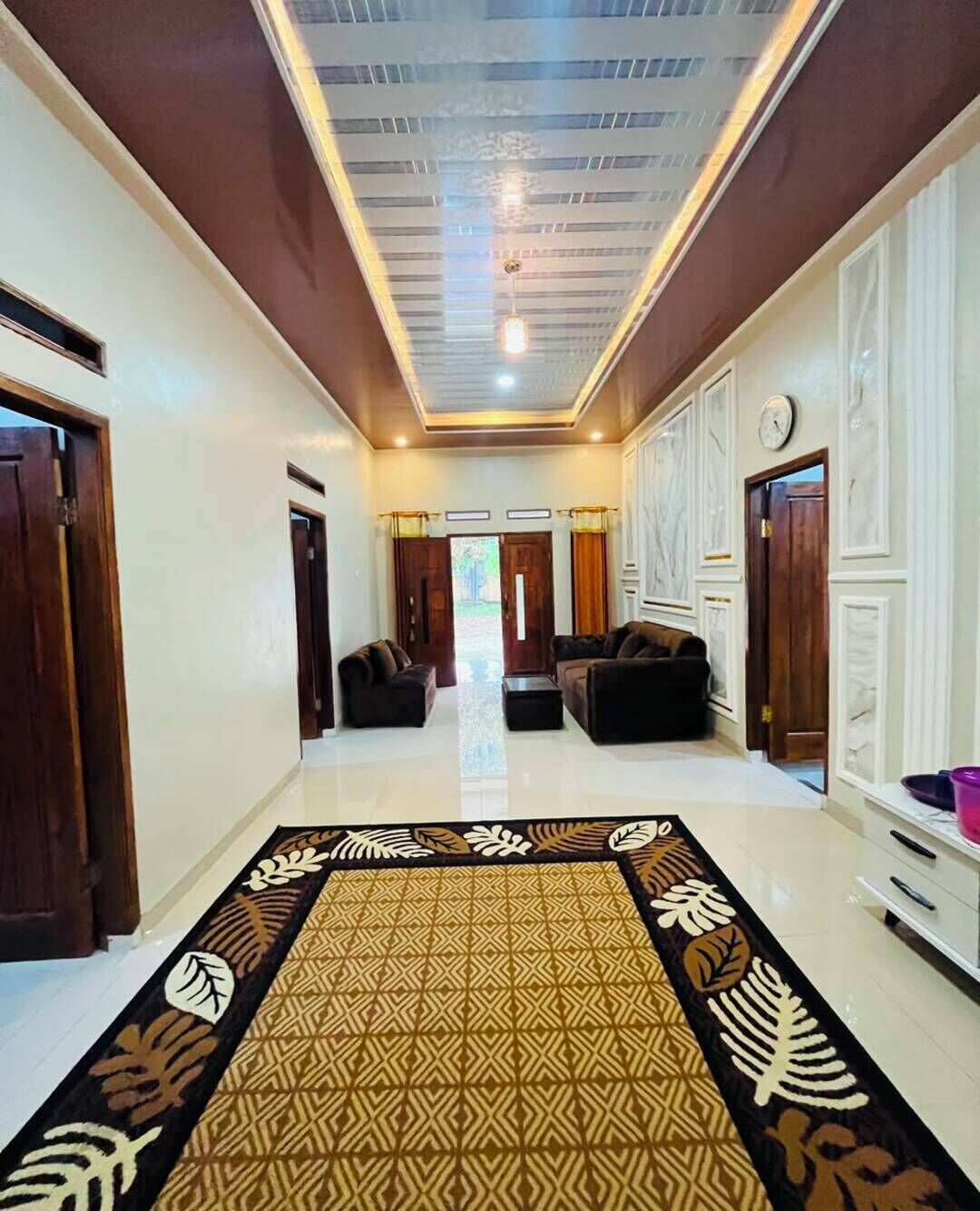Un pasillo con alfombra estampada, un sofá y un reloj en la pared.