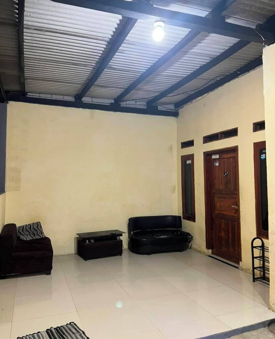 A room with a tiled floor, a black sofa, a black cabinet, and a wooden door.
