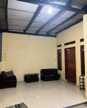 A room with a tiled floor, a black sofa, a black cabinet, and a wooden door.