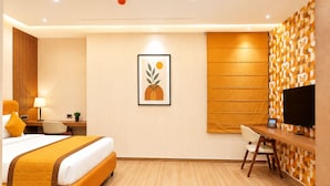 Une chambre d’hôtel avec un lit, un bureau, une chaise, une télévision et un tableau encadré au mur.
