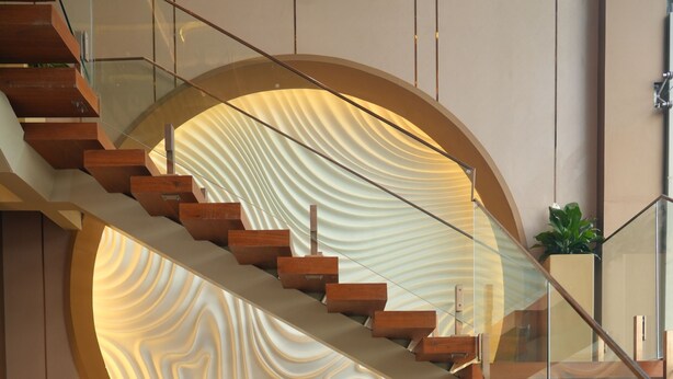 Un intérieur moderne avec un escalier à volutes, un coin salon doté de coussins orange et un mur orné d’un motif lumineux original.