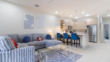 A modern living room with a sofa, a glass coffee table, and a blue rug.