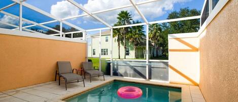 A pool area with a glass enclosure, two chairs, and a pink float.