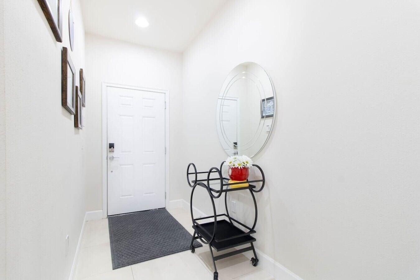 A hallway with a white door, a black metal cart with a vase of flowers, and a large mirror on the wall.