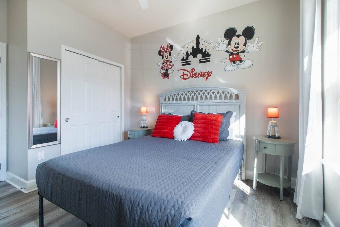 Une chambre d’hôtel avec un lit, une table de chevet, un miroir et des œuvres d’art murales sur le thème de Disney.
