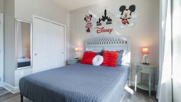 A hotel room with a bed, a nightstand, a mirror, and Disney-themed wall art.