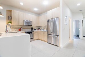A modern kitchen with stainless steel appliances, a central island, and light wood cabinetry. - Mickeys Hideaway |Mins to Disney, Private Pool (Clermont)