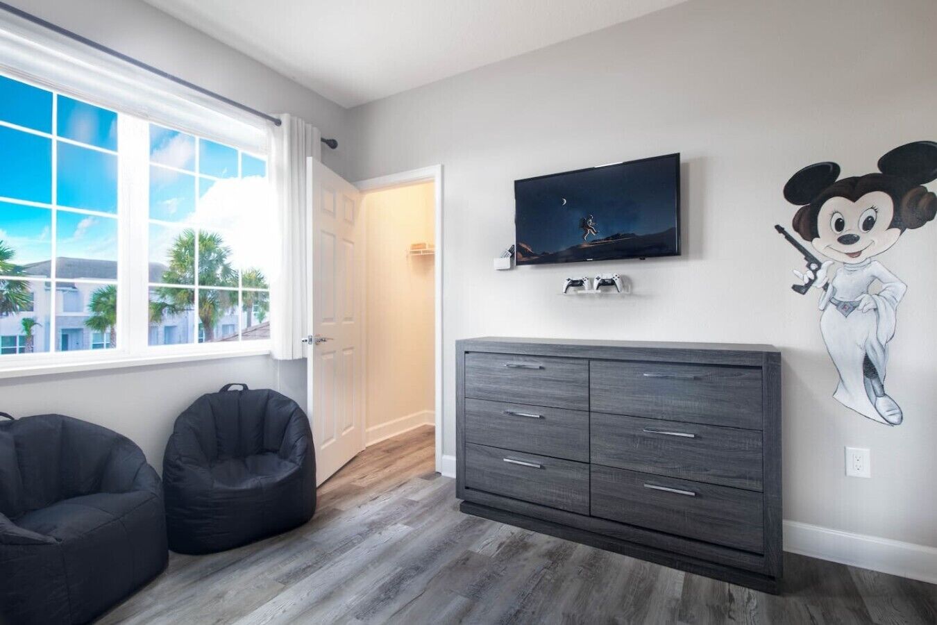 A room with a large window, a television, a dark-colored cabinet, and a wall mural.
