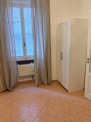 Ein Zimmer mit Heizkörper, Kleiderschrank und einem Fenster mit Vorhängen.
