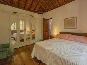 Quarto com cama, guarda-roupa, cadeira e porta que dá para outro espaço.