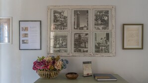 Ein Zimmer mit einer antiken Wanduhr, einem gerahmten Foto und einem kleinen Tisch mit Blumen in einer Vase.
