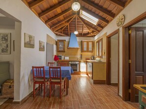 Una cuina amb armaris de fusta, una taula de dinar amb caires i un rellotge a la paret.