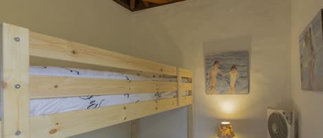 A bunk bed room with a wooden ceiling, a bedside table with a lamp, and a wall painting.