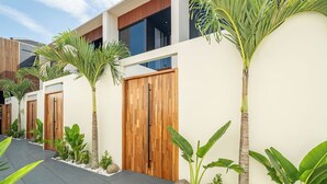A modern building with a wooden door, surrounded by tropical plants and a paved walkway. - Chic 2BR Umalas Villa with Workspace (Badung)