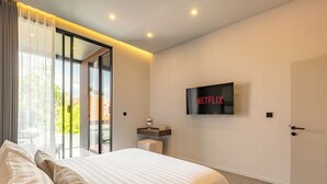 A modern hotel room with a large bed, a TV mounted on the wall, and a sliding glass door leading to an outdoor area. - Chic 2BR Umalas Villa with Workspace (Badung)