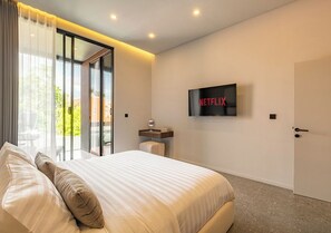 Ein modernes Hotelzimmer mit einem großen Bett, einem an der Wand montierten Fernseher und einer Glasschiebetür zu einem Außenbereich.