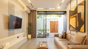 A modern living room with a flat-screen TV, a sofa, a coffee table, and a sliding glass door leading to an outdoor area. - Chic 2BR Umalas Villa with Workspace (Badung)