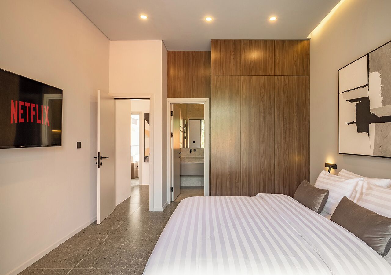 Una camera da letto moderna con un letto grande, una parete decorata in legno, una TV a parete e un corridoio che conduce al bagno.
