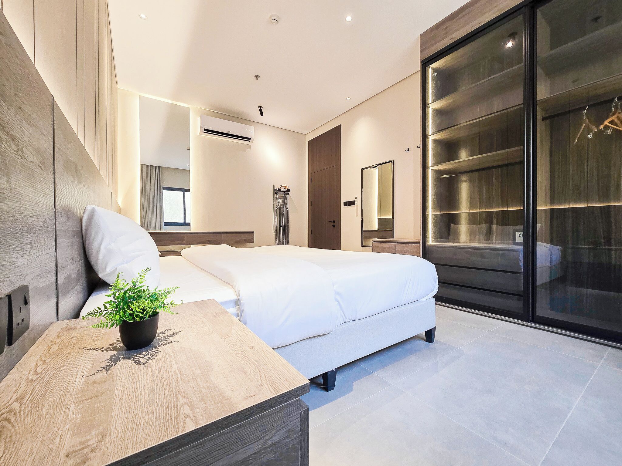 A modern bedroom with a bed, bedside table, and a large mirror.