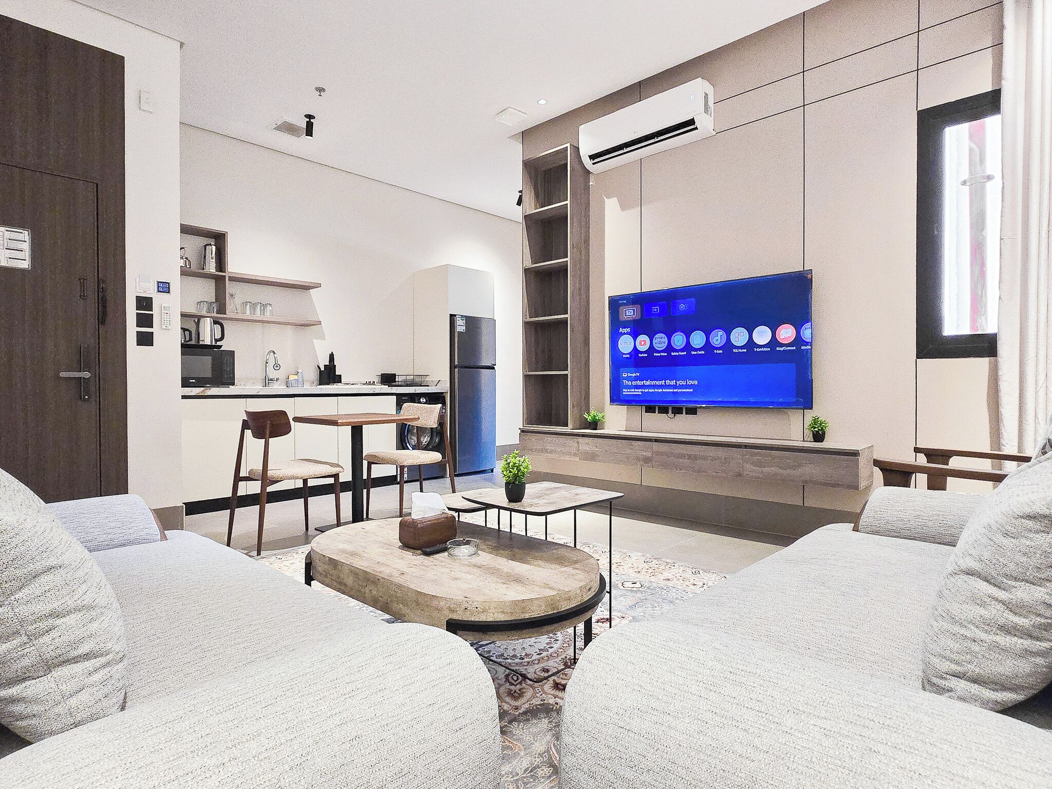 A modern living room with a flat-screen TV, a dining area with a kitchen in the background, and a cozy seating area with a coffee table.
