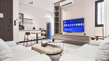 A modern living room with a flat-screen TV, a dining area with a kitchen in the background, and a cozy seating area with a coffee table.