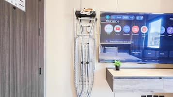 Un salón moderno con un televisor de pantalla plana montado en la pared, un soporte metálico con una planta y un mueble bajo de madera.