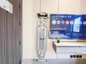 Un salón moderno con un televisor de pantalla plana montado en la pared, un soporte metálico con una planta y un mueble bajo de madera.