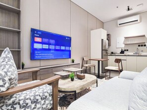 Una habitación de hotel moderna con una televisión de pantalla plana mostrando la pantalla de inicio, una kitchenette, una zona de estar con una mesa redonda y un sofá.