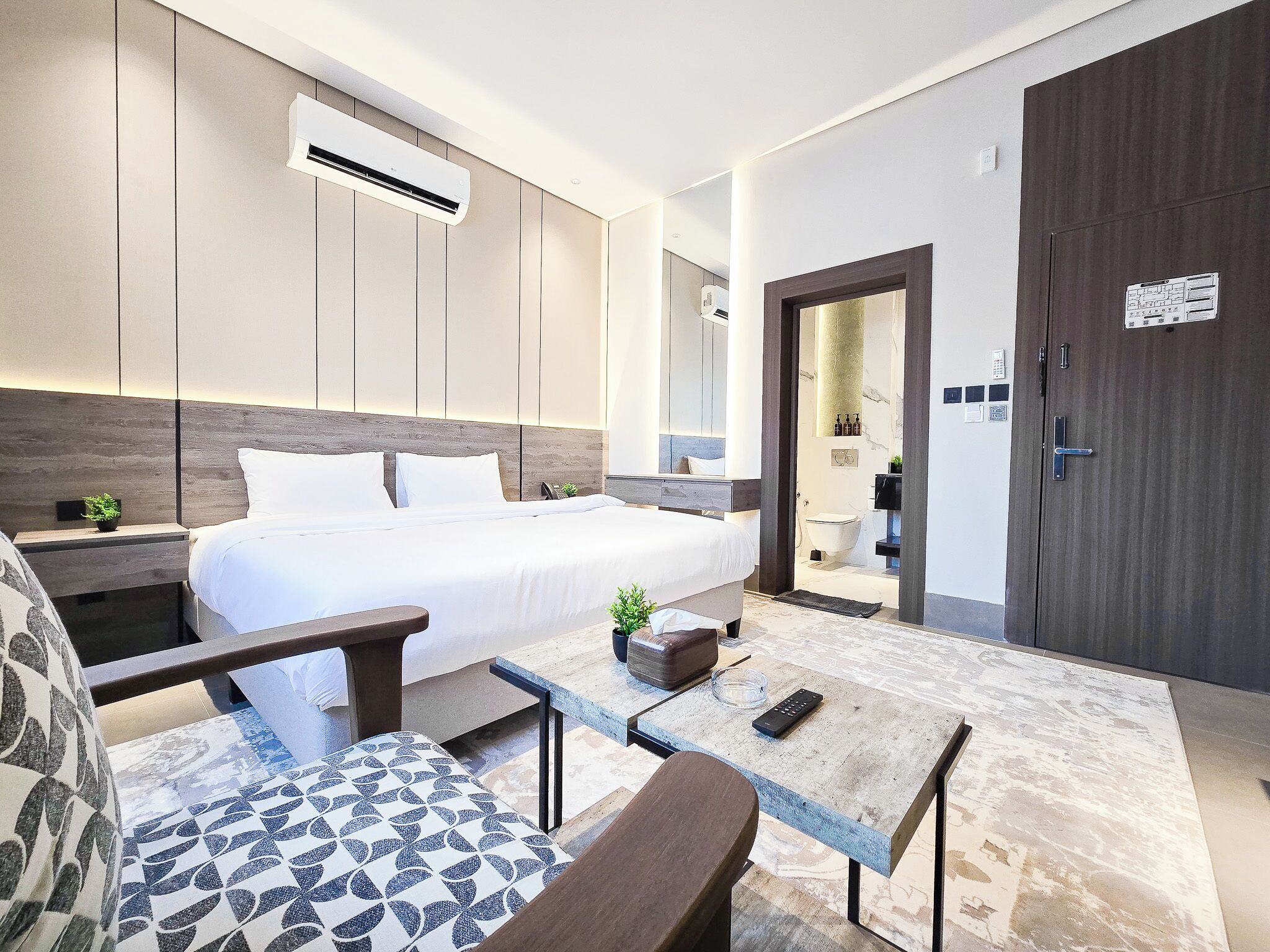 A modern hotel room with a bed, bedside tables, a desk, and a seating area.