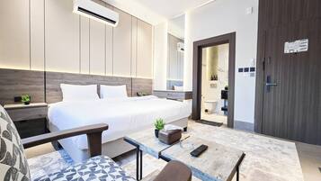 A modern hotel room with a bed, bedside tables, a desk, and a seating area.
