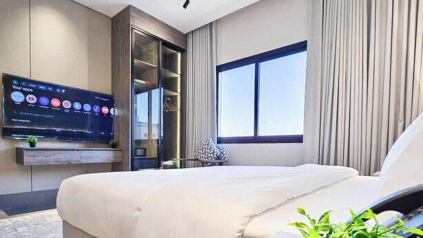 A modern hotel room with a large bed, a flat-screen TV mounted on the wall, a large window with curtains, and a small plant on the bedside table. - MR STAY (Riyadh)