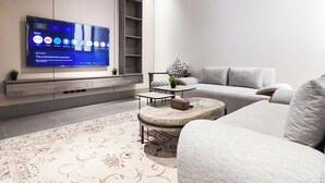 A modern living room with a flat-screen TV mounted on the wall, a grey sofa, a patterned rug, and a small coffee table. - MR STAY (Riyadh)