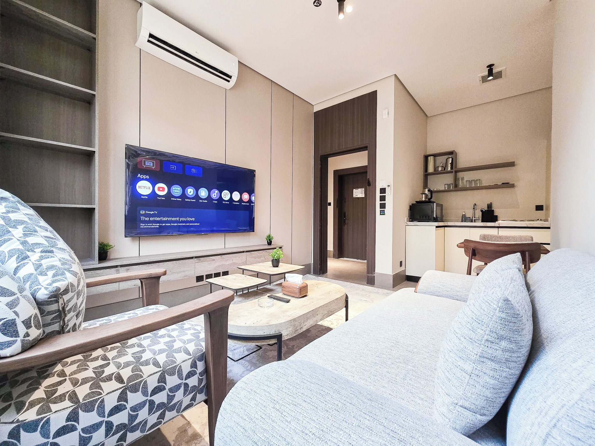 Uma sala de estar moderna com televisão de tela plana, assentos e um espaço de cozinha compacto.