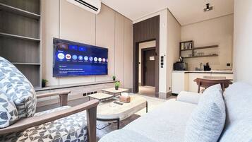Uma sala de estar moderna com televisão de tela plana, assentos e um espaço de cozinha compacto.