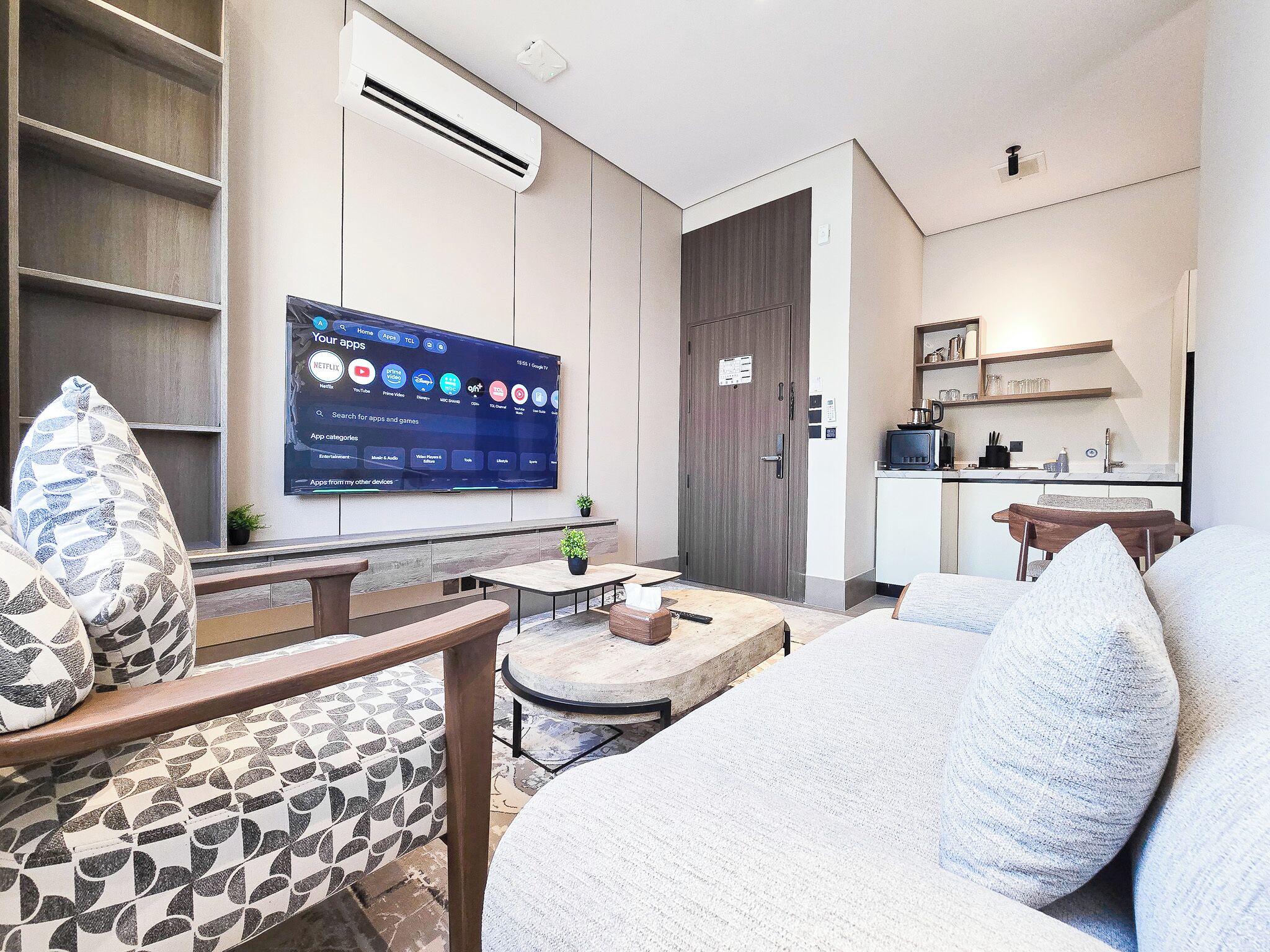 Una sala moderna con un televisor de pantalla plana montado en la pared, un sofá, una mesa de centro y un sillón estampado.