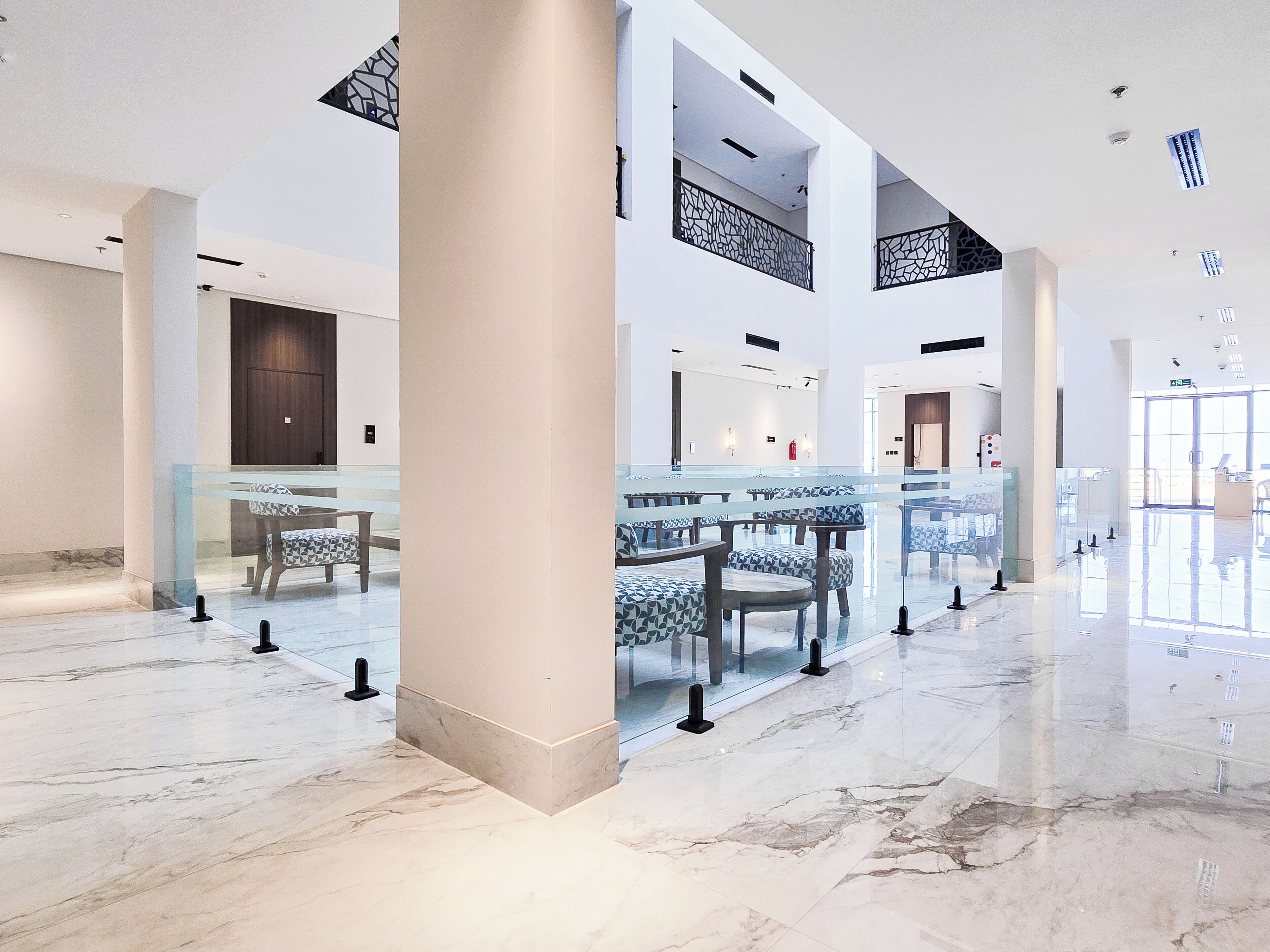 A spacious lobby with marble flooring, glass partitions, and modern furniture.