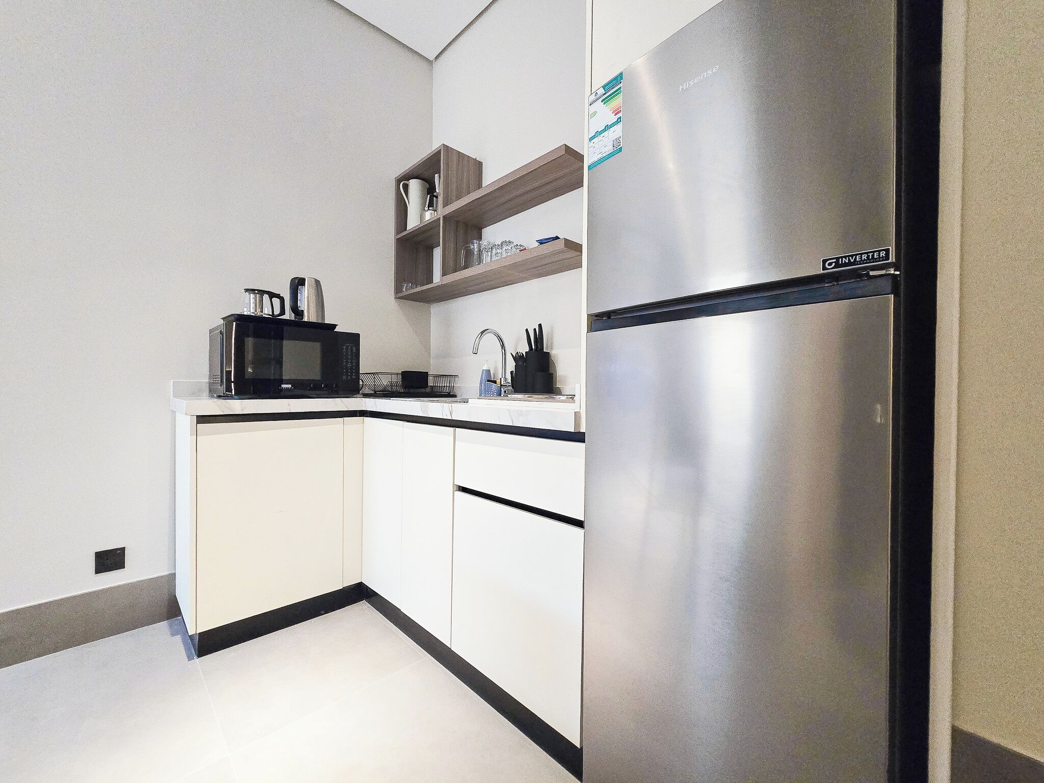 A modern kitchen with white cabinetry, a stainless steel refrigerator, a microwave, and a sink.