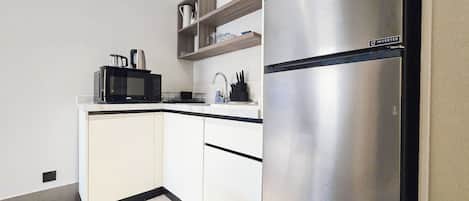 Una cocina moderna con armarios blancos, un refrigerador de acero inoxidable, un microondas y un lavamanos.