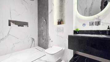 A modern bathroom with a marble floor, a black sink, a white toilet, and a shower area.