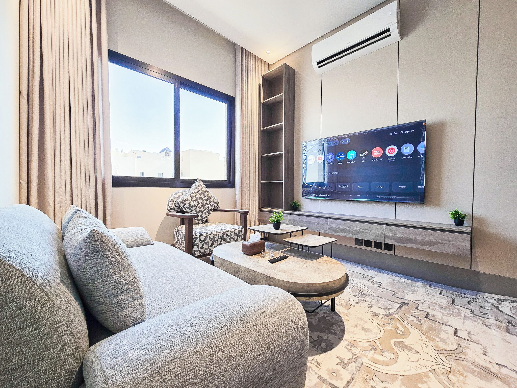 A modern living room with a large flat-screen TV mounted on the wall, a sofa, a coffee table, and a small side table with a plant.