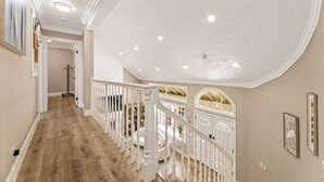 Um interior espaçoso com escada de madeira, guarda-corpos brancos e um alto teto com iluminação embutida.