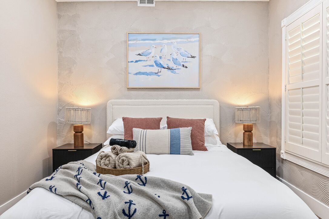 Een slaapkamer met een groot bed, twee nachtkastjes, een schilderij aan de muur en een raam met luiken.